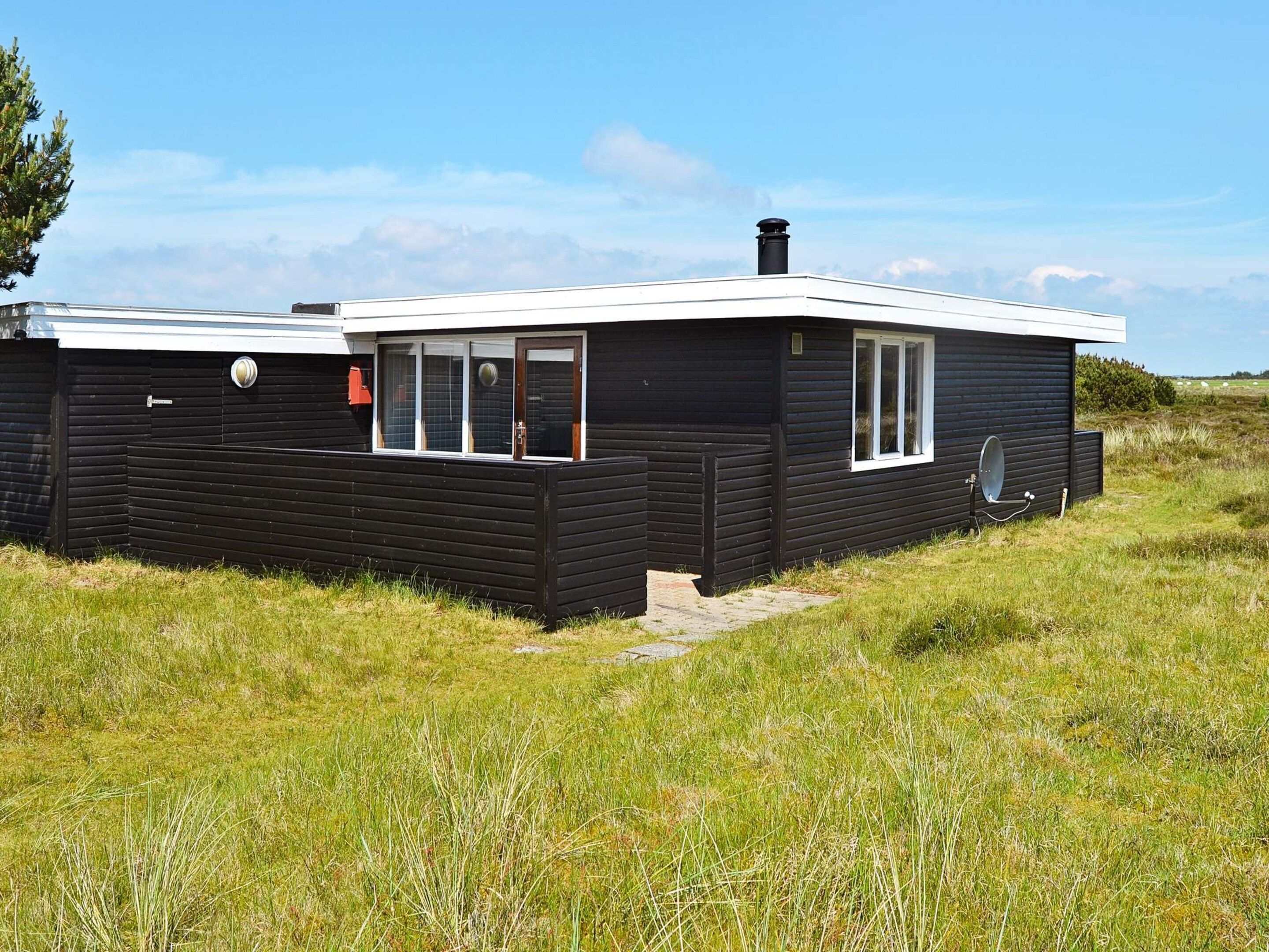A black wooden house with a white roof, a satellite dish, and a chimney.