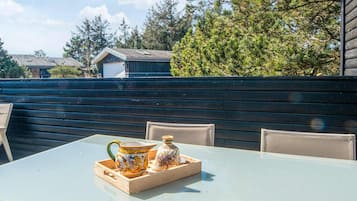 Un patio al aire libre con una mesa de vidrio, dos sillas y contenedores de cerámica sobre una bandeja de madera.