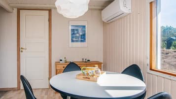 Una habitación con una mesa redonda, sillas, una lámpara colgante blanca, un equipo de aire acondicionado, un armario de madera y un cuadro en la pared.