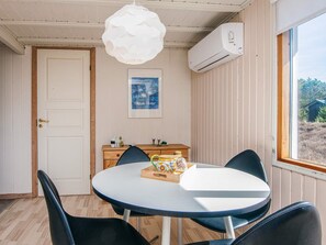 Une pièce comprenant une table ronde, des chaises, un luminaire suspendu blanc, un appareil de climatisation, un meuble en bois et un tableau encadré accroché au mur.