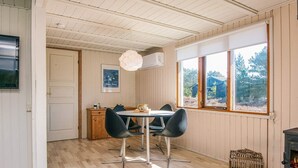 A dining area with a table and chairs, a wooden cabinet, a framed picture, and a window with a view of trees. - Child Friendly Holiday Home in Fanø near Sea (Fano)