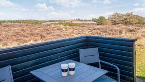 An outdoor seating area with a table and chairs, overlooking a dry landscape with sparse vegetation and a distant red building. - Child Friendly Holiday Home in Fanø near Sea (Fano)