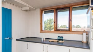 A kitchen with white cabinets, a black countertop, and a window with a view of trees and buildings. - Child Friendly Holiday Home in Fanø near Sea (Fano)