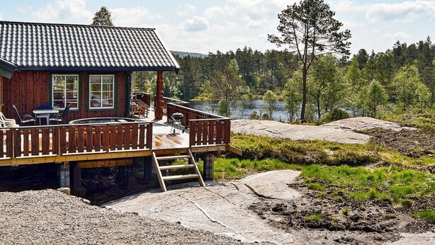 Una cabaña de madera con terraza, asientos exteriores y vistas a un área boscosa.