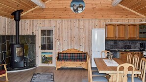 Un acogedor interior de cabaña con chimenea de piedra, mesa de comedor de madera y zona de cocina.