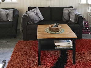 A living room with a dark sofa, a wooden coffee table, and a red rug. - Holiday Home in Sölvesborg (Sölvesborg)