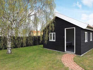 A black house with a white door and windows, surrounded by a grassy yard and a tree.