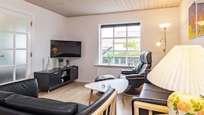 Un salon moderne doté d’un téléviseur à écran plat, de canapés en cuir noir, d’une table basse en bois et d’une grande fenêtre offrant une vue sur l’extérieur.