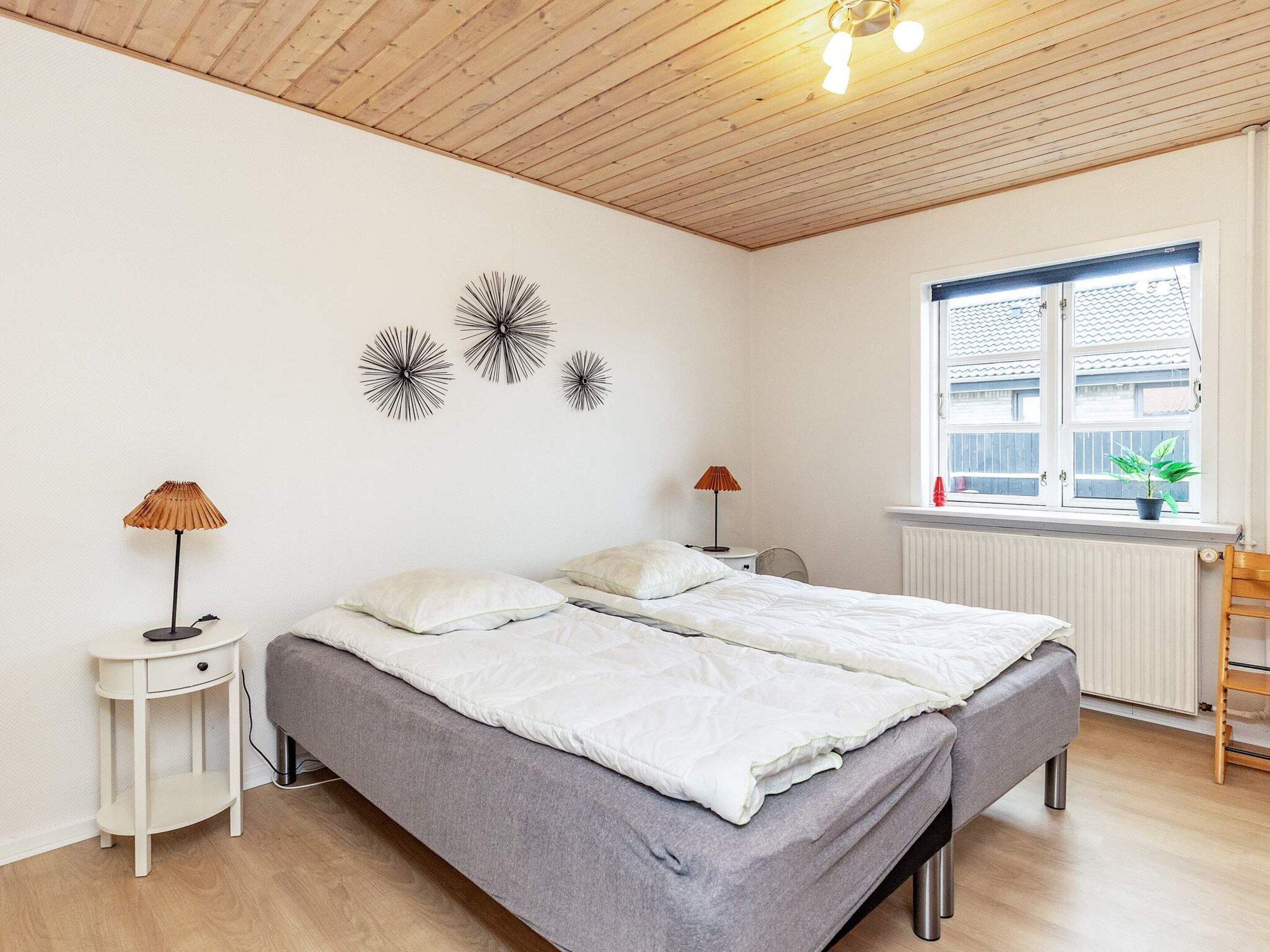 A bedroom with a bed, two bedside tables, a radiator, a window with a view, and wall art.