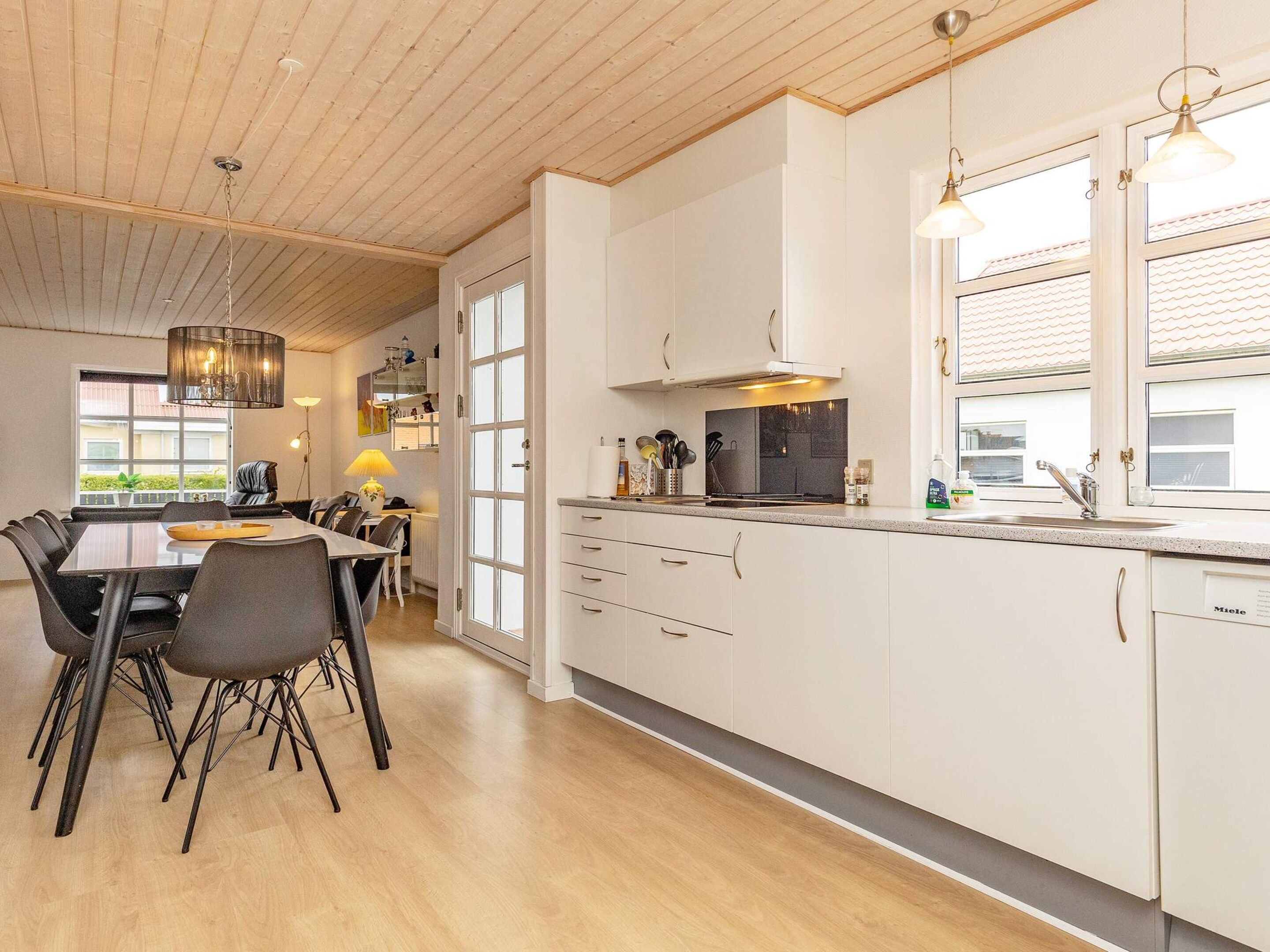 A modern kitchen with white cabinets, a dining area with a table and chairs, and a wooden ceiling.