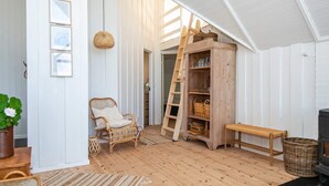 Una stanza accogliente con pavimento in legno, una sedia in vimini, una panca, una scala e un armadietto in legno con scaffali.