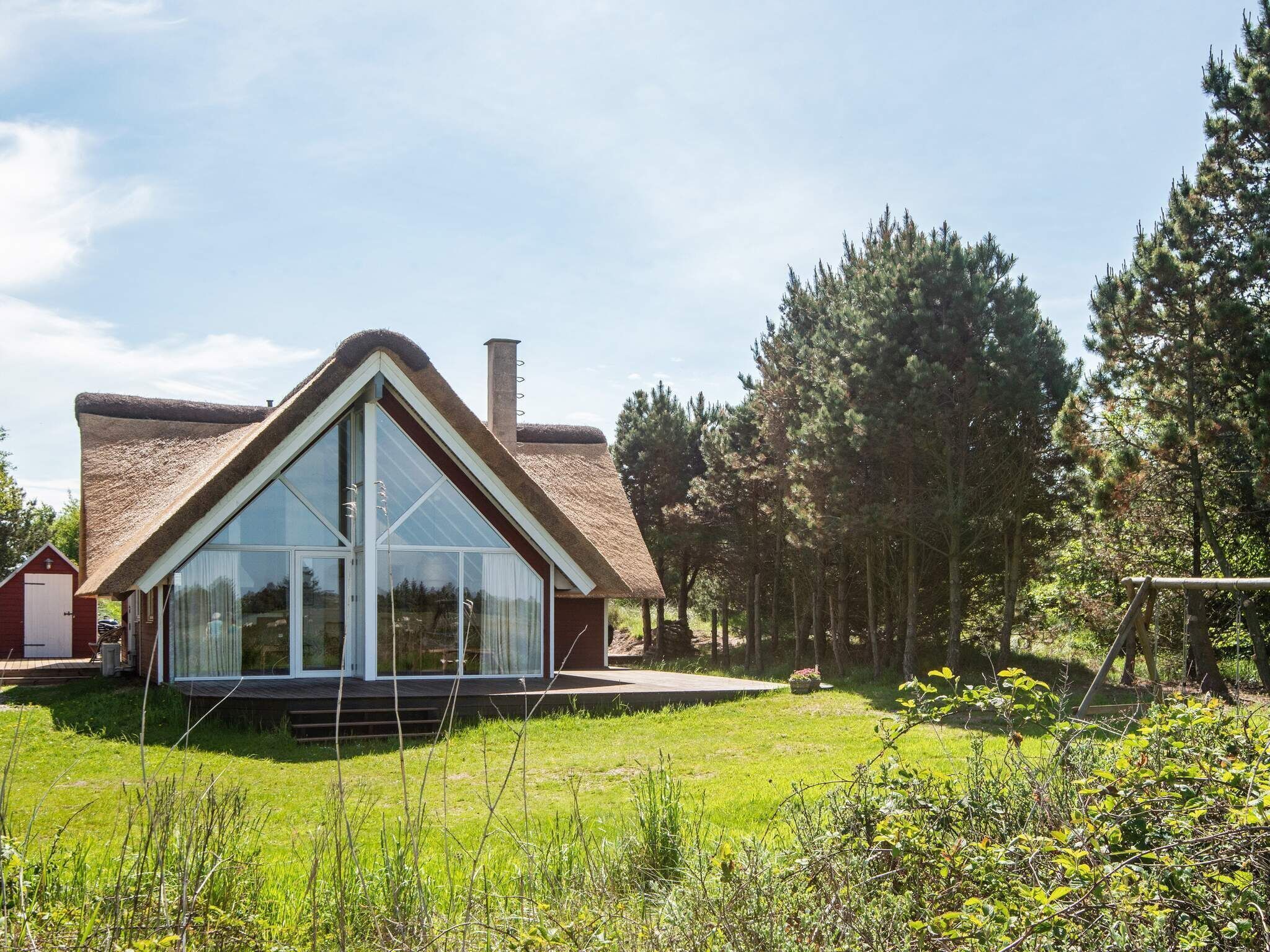 Una casa moderna con un amplio ventanal, rodeada de un jardín cubierto de césped y árboles altos.