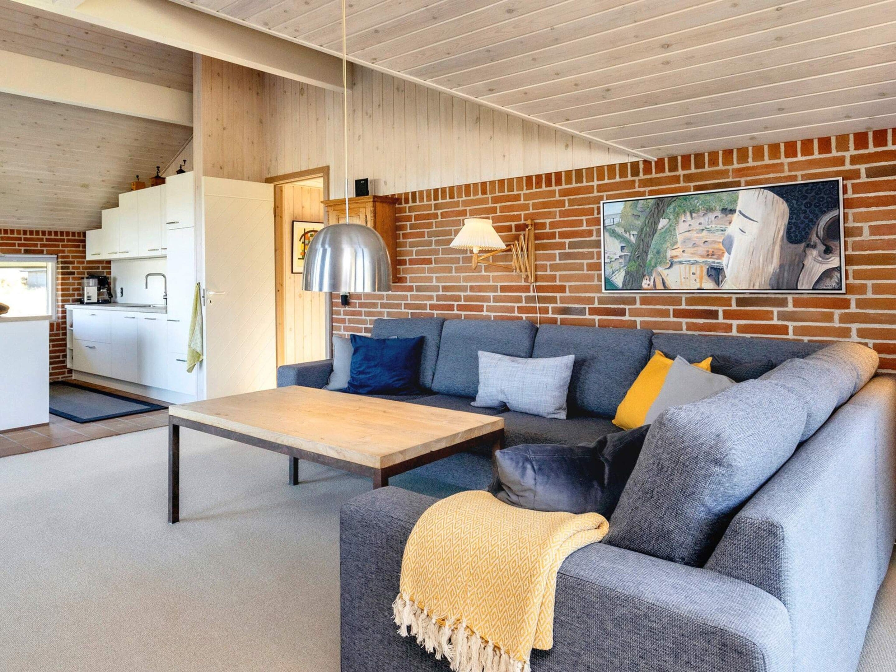 A modern living room with a grey sofa, a wooden coffee table, and a kitchen in the background.