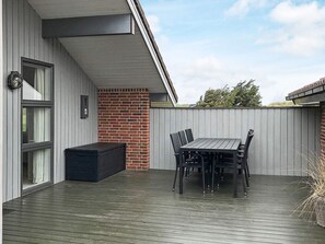 A covered outdoor patio with a table and chairs, a black storage bench, and a brick wall.