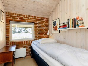 A bedroom with a brick wall, a window, a bed, a desk, and a bookshelf.
