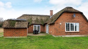 A brick house with a thatched roof, a small attached structure, and a patio area with outdoor furniture. - 10 Person Holiday Home in Ulfborg (Ulfborg)