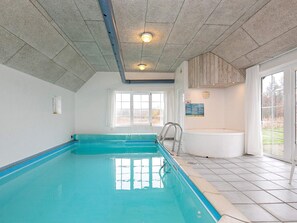 Une piscine intérieure avec un sol carrelé, une fenêtre et un plafond en bois.