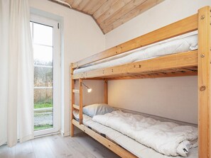 A bunk bed with a wooden frame, a bedside lamp, and a view through a window to the outdoors.