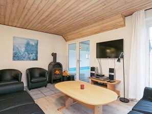 Un salon chaleureux avec un plafond en bois, une cheminée, un téléviseur et un canapé.