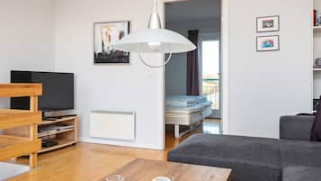Ein modernes Wohnzimmer mit Fernseher, einer Couch, einem Couchtisch und einem Bett im angrenzenden Zimmer.