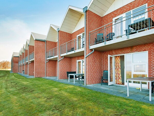 A row of brick buildings with balconies, outdoor seating, and a grassy area.