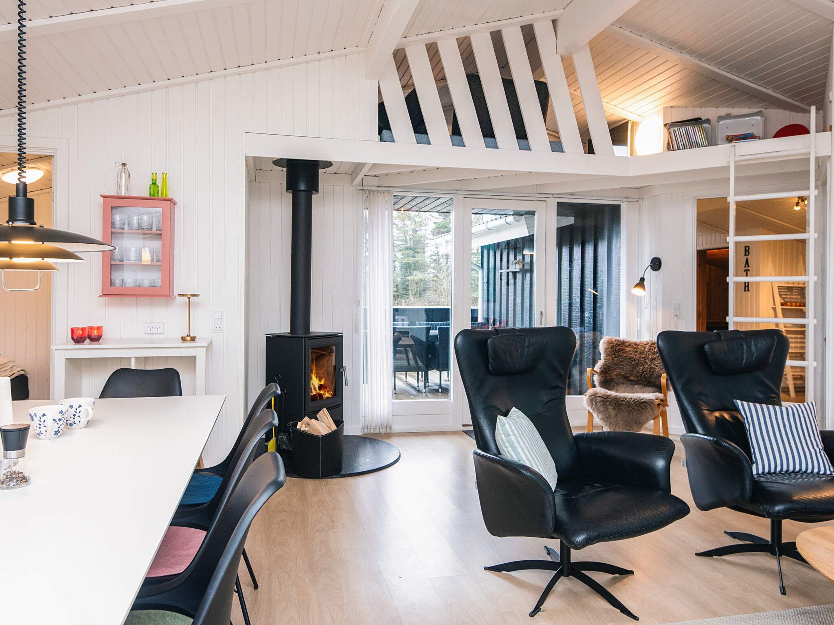 Un interior moderno con una chimenea central, sillones de cuero negro, una mesa de comedor y un techo blanco con vigas de madera.
