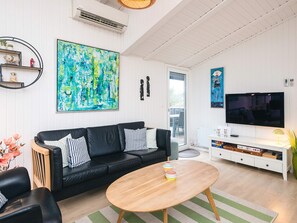 A modern living room with a black leather sofa, a wooden coffee table, and a large abstract painting.