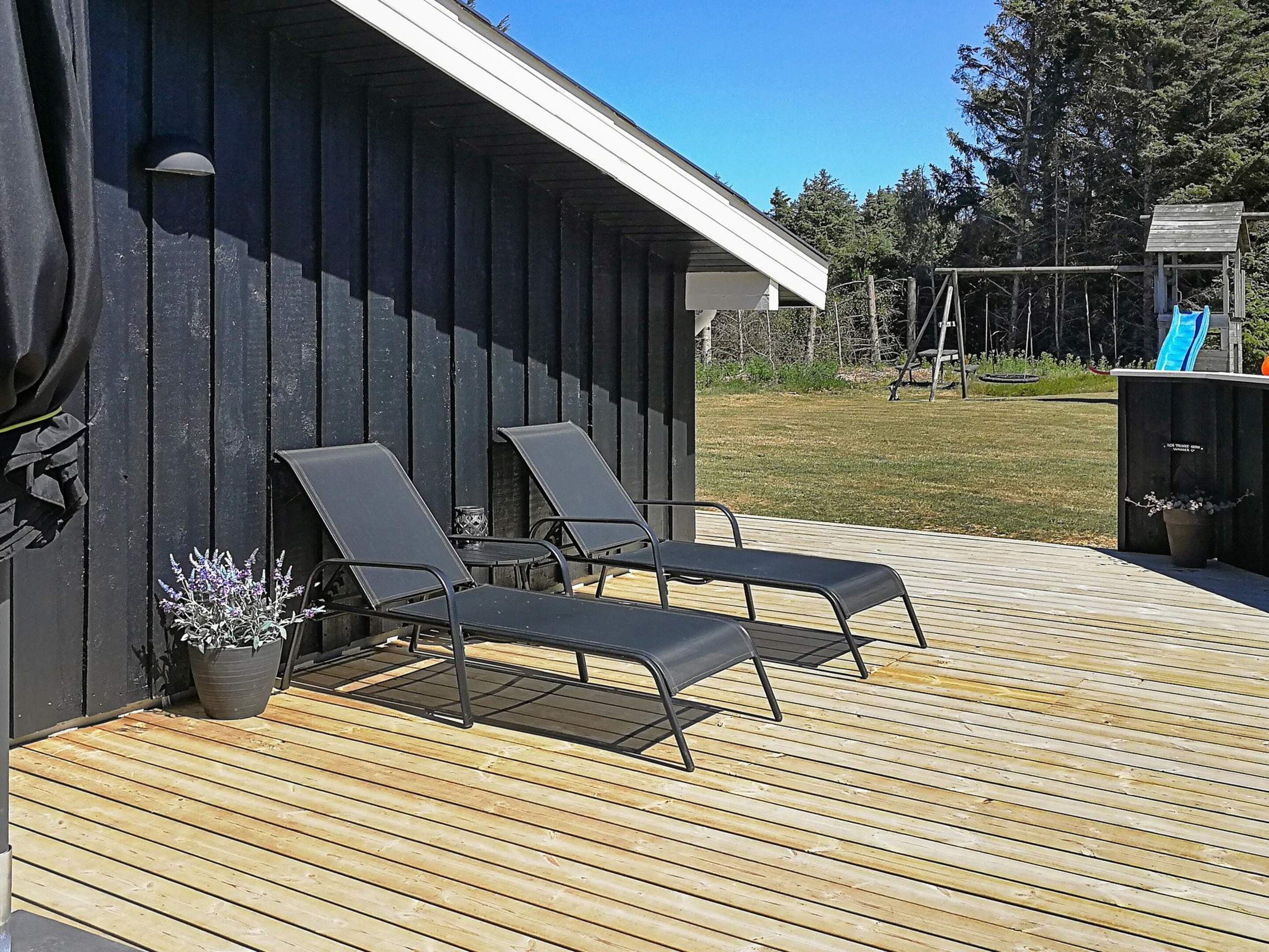 A wooden deck with two lounge chairs and a potted plant.