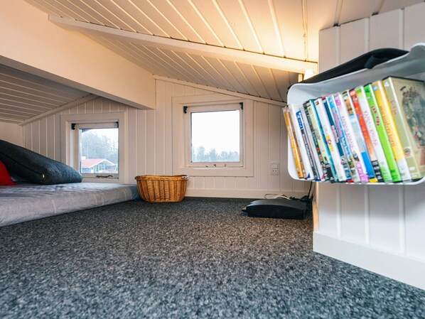 A cozy attic bedroom with a sloped ceiling, a window, a bookshelf, a mattress, and a woven basket.