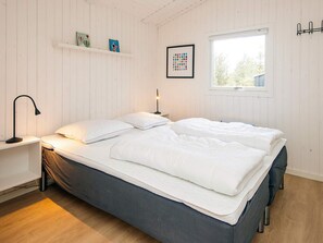 A bedroom with a bed, bedside tables, a lamp, a window, and a wall-mounted shelf with books.