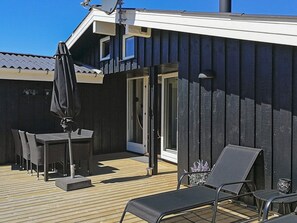 Une terrasse dotée de mobilier d’extérieur, comprenant des chaises et une table, et une porte-fenêtre coulissante donnant sur un espace intérieur.