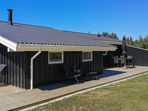 A wooden deck with a covered outdoor seating area, a chimney, and a view of the surrounding landscape.