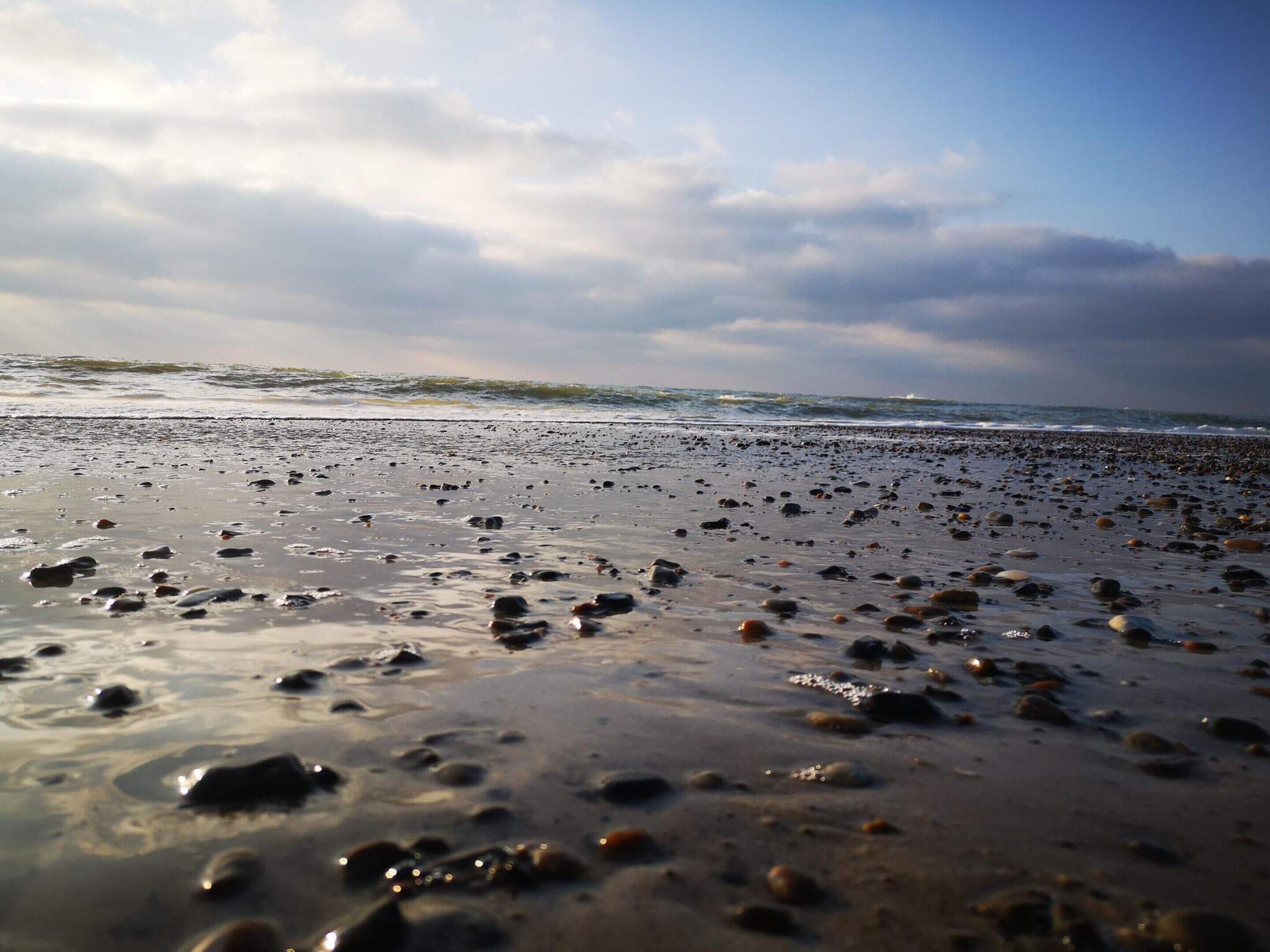 Een strand met een uitgestrekte zandvlakte en verspreide rotsen, dat uitloopt in de oceaan.