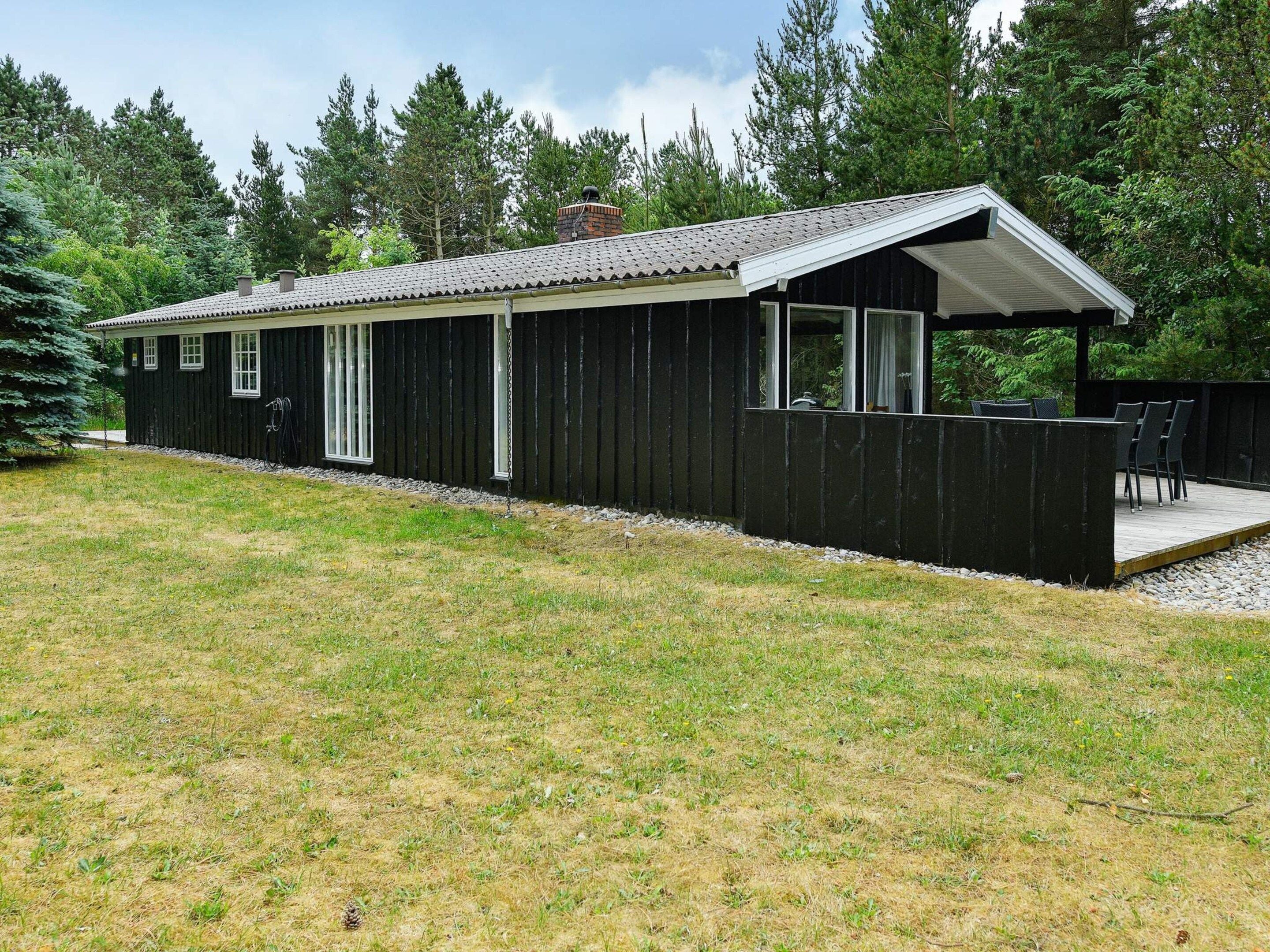 A single-story wooden building with a covered porch, a small deck, and a grassy yard.