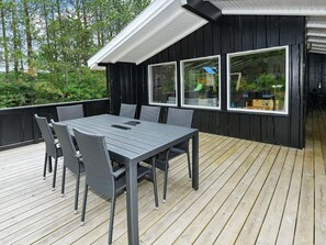 Une terrasse avec une table et des chaises, de grandes fenêtres et une vue sur la verdure.