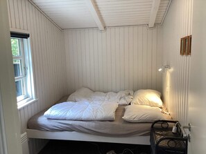 A single bed with a headboard, a bedside table with a lamp, and a window with blinds. - 6 Person Holiday Home in Norre Nebel (Norre Nebel)