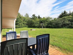 An outdoor patio with a table and chairs, a swing set, and a grassy yard. - 6 Person Holiday Home in Bindslev (Bindslev)