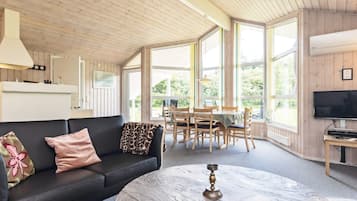 En hyggelig stue med en sort sofa, et rundt sofabord i marmor og et spiseområde med træstole og et bord.