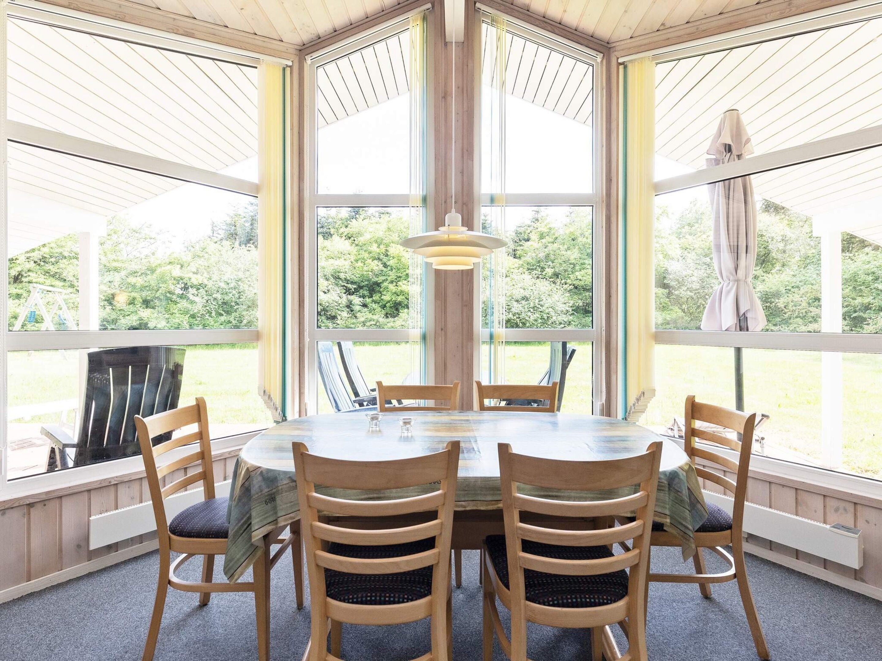 A dining area with a round table and six chairs, large windows, and a hanging light fixture.