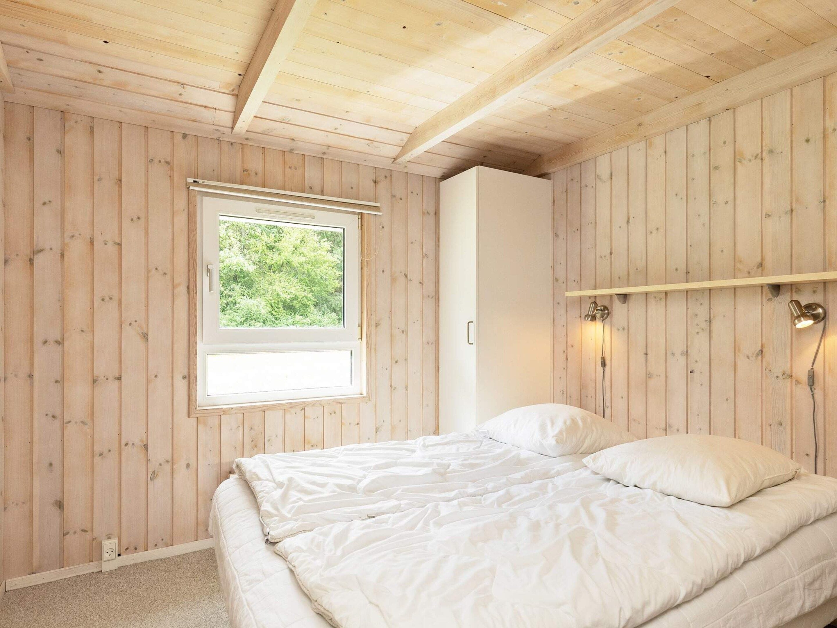 A bedroom with a bed, a window, a wardrobe, and a wall-mounted light fixture.