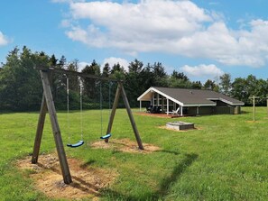 A wooden swing set in a grassy field with a covered structure in the background. - 6 Person Holiday Home in Bindslev (Bindslev)