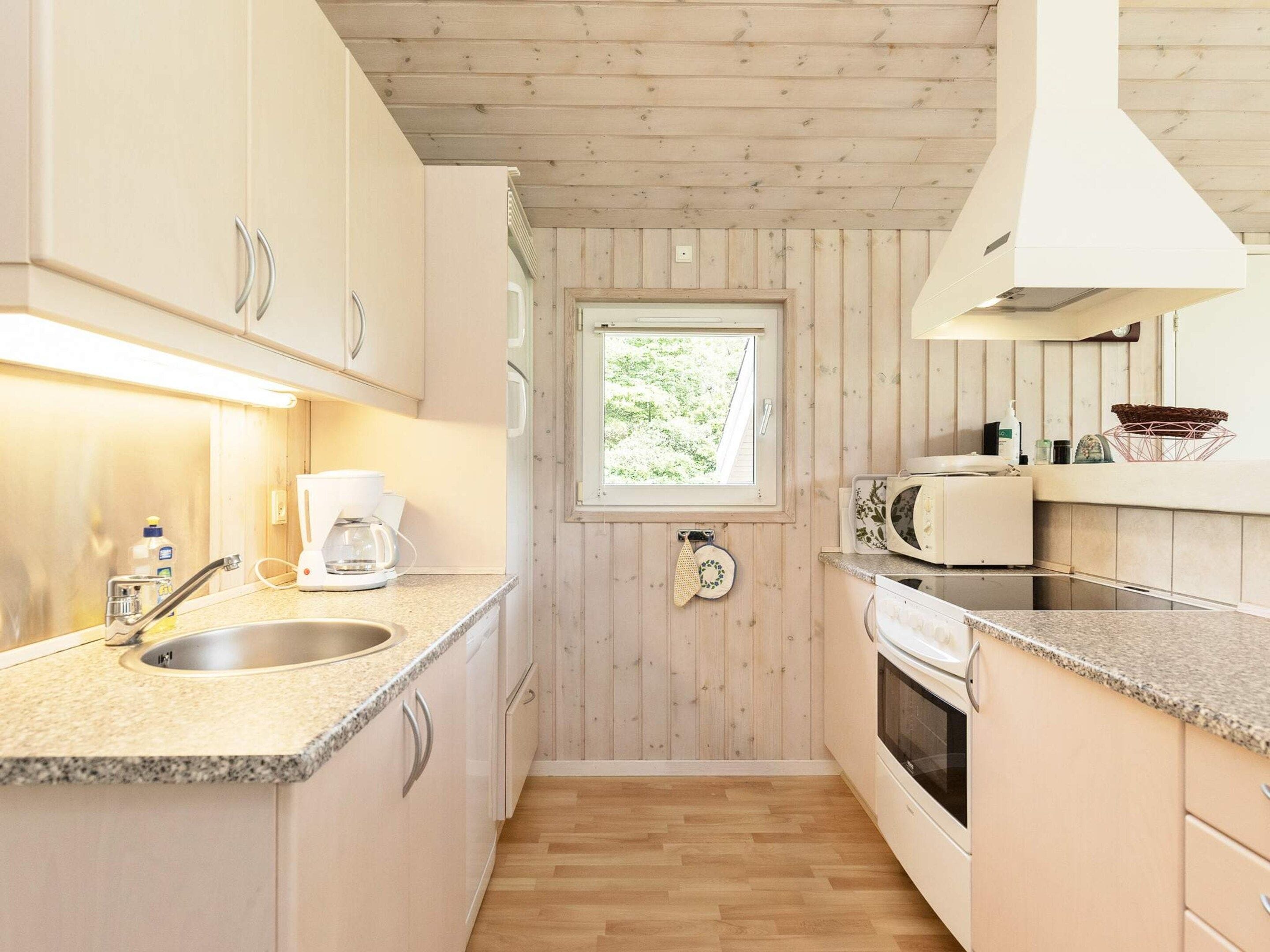 A compact kitchen with a window, wooden cabinets, a sink, a coffee maker, and a microwave.