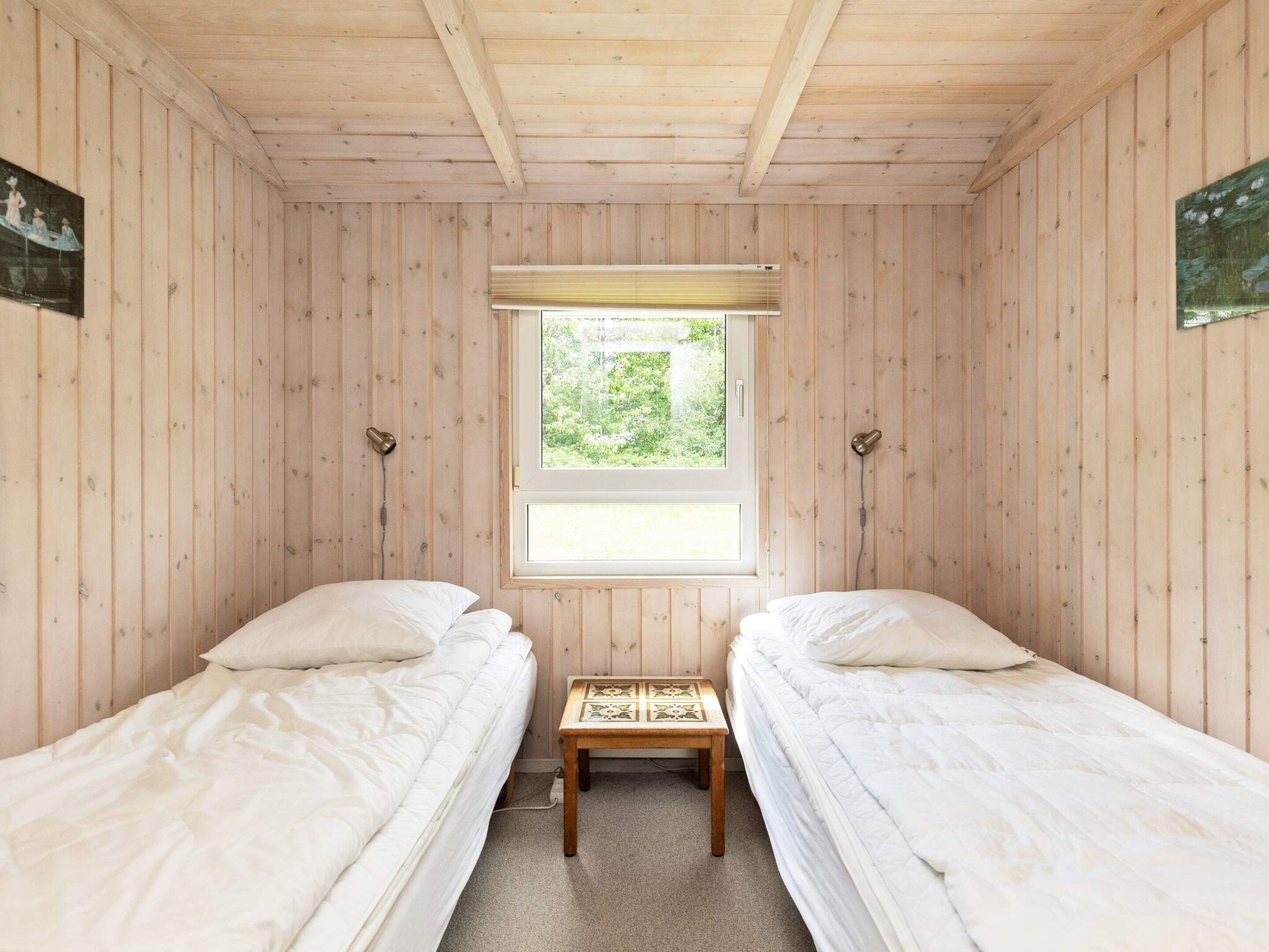 Habitación con dos camas individuales, ventana con vista a vegetación y paredes de madera.