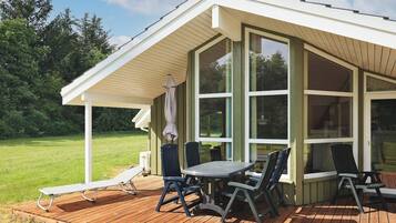 A covered outdoor patio with a table and chairs, a cushioned lounge chair, and a pergola with an umbrella.