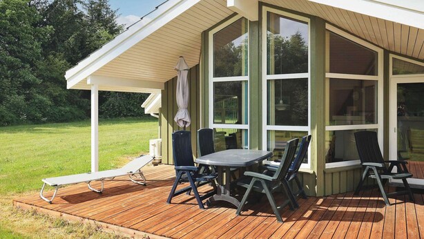 A covered outdoor patio with a table and chairs, a cushioned lounge chair, and a wooden deck. - 6 Person Holiday Home in Bindslev (Bindslev)