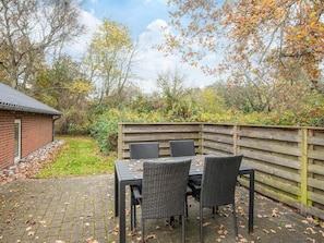 A patio with a table and chairs, surrounded by a wooden fence and a brick building.