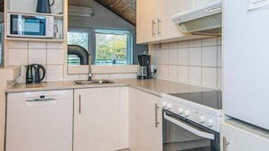 A compact kitchen with white cabinets, a microwave, a kettle, a coffee maker, and a stove. - 4 Star Holiday Home in Glesborg (Glesborg)