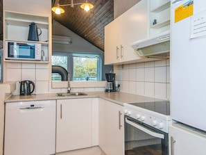 A compact kitchen with white cabinets, a microwave, a kettle, a coffee maker, and a stove.