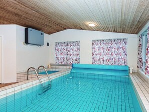 An indoor swimming pool with tiled walls, a wooden ceiling, and a blue pool edge. - 4 Star Holiday Home in Glesborg (Glesborg)
