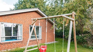A wooden swing set in front of a brick house with a window and a red bucket. - 4 Star Holiday Home in Glesborg (Glesborg)